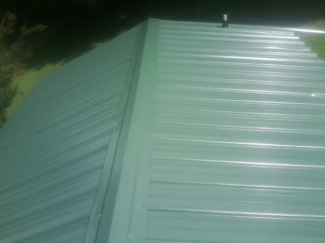 New green metal panels meeting at the ridge of a roof — Flat Roof Repair work by our crew in Lindsay