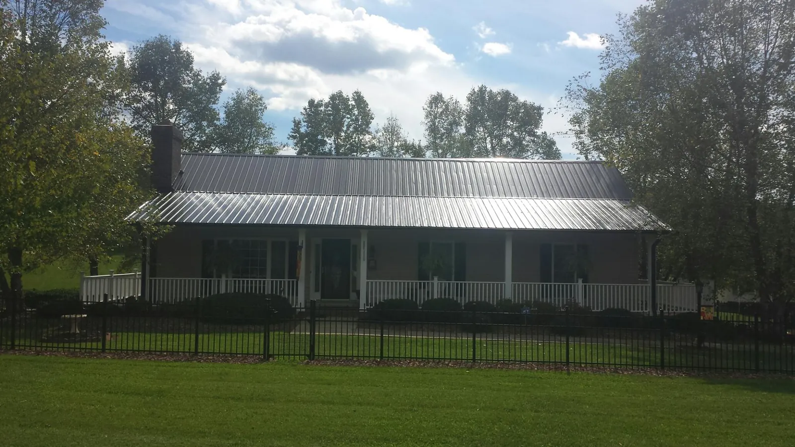 Gray metal roof on a brick ranch with a full width front porch — Gutter Guard Installation work by our crew in Lindsay