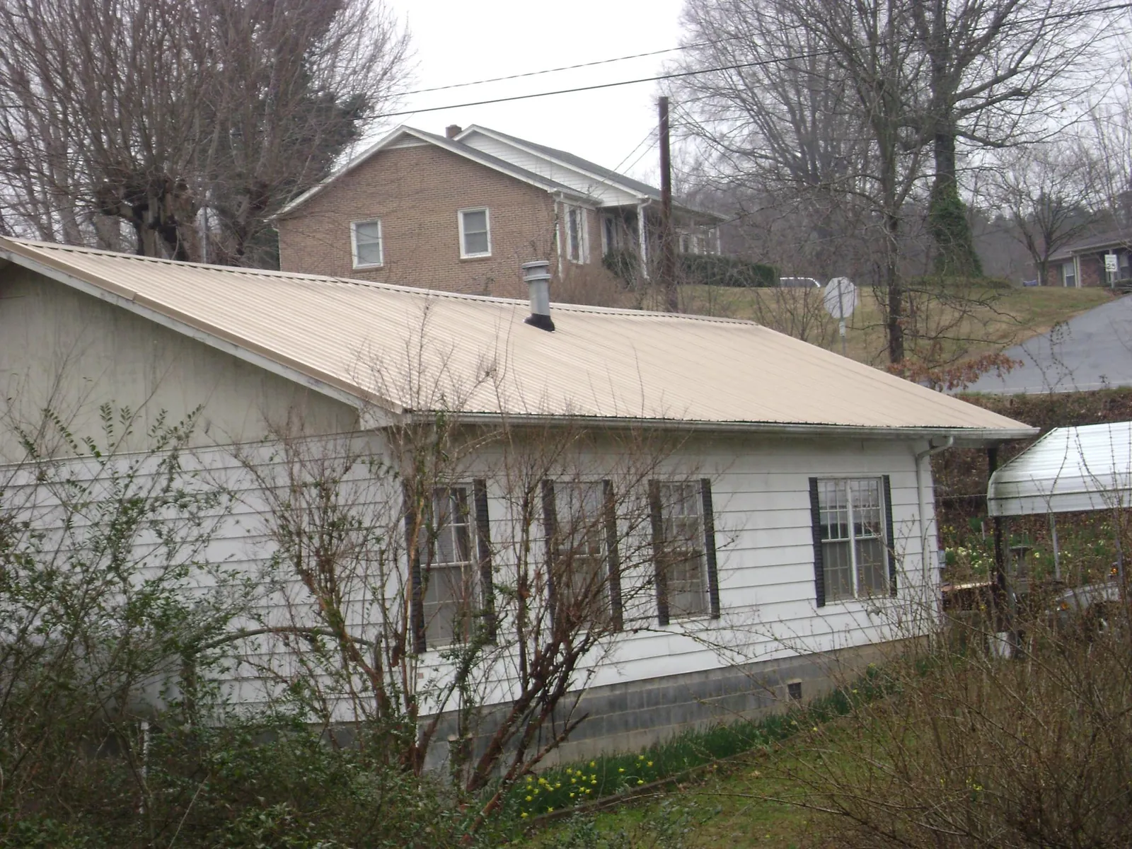 Tan metal roof on a white sided house set into a hillside — Commercial Roofing by Roofing Brothers in Lindsay