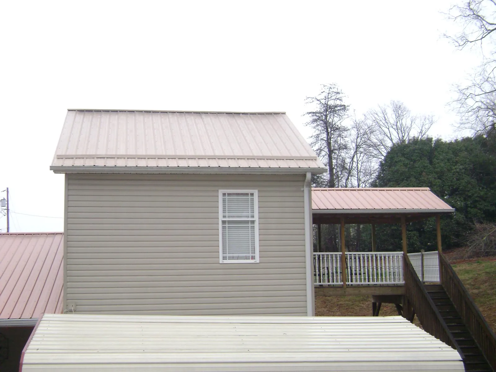 Tan metal roofs on a two story addition and attached porch, from a Roof Replacement job in Lindsay